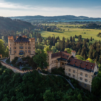 Schloss Hohenschwangau Das prächtige Schloss Hohenschwangau thront auf einem Hügel inmitten einer grünen Landschaft. Die Aussicht bietet eine idyllische Kulisse.