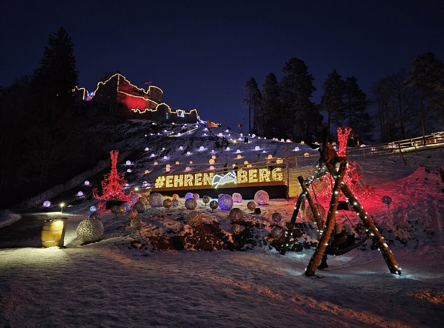 Das Bild zeigt eine Burgruine bei Nacht, die in bunten Farben beleuchtet ist. Es liegt Schnee.