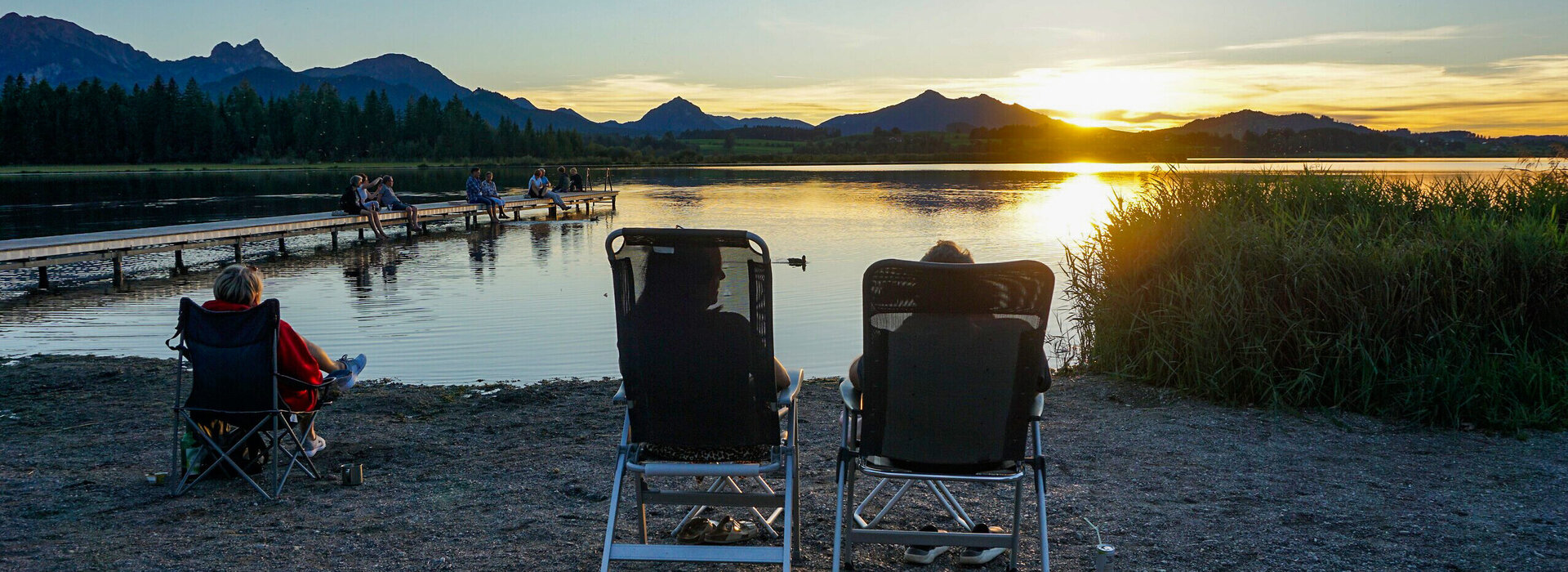 Ein Pärchen genießt den Sonnenuntergang auf Campingstühlen am Hopfensee im Allgäu