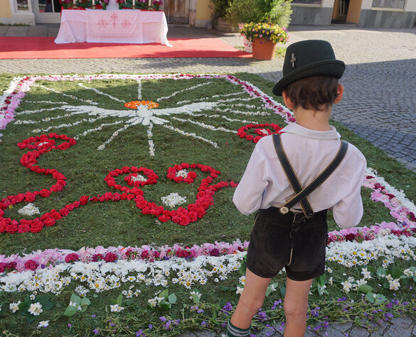 Ein Bub in Tracht steht vor dem Fronleichnams-Blumenteppich auf dem Schrannenplatz in Füssen.