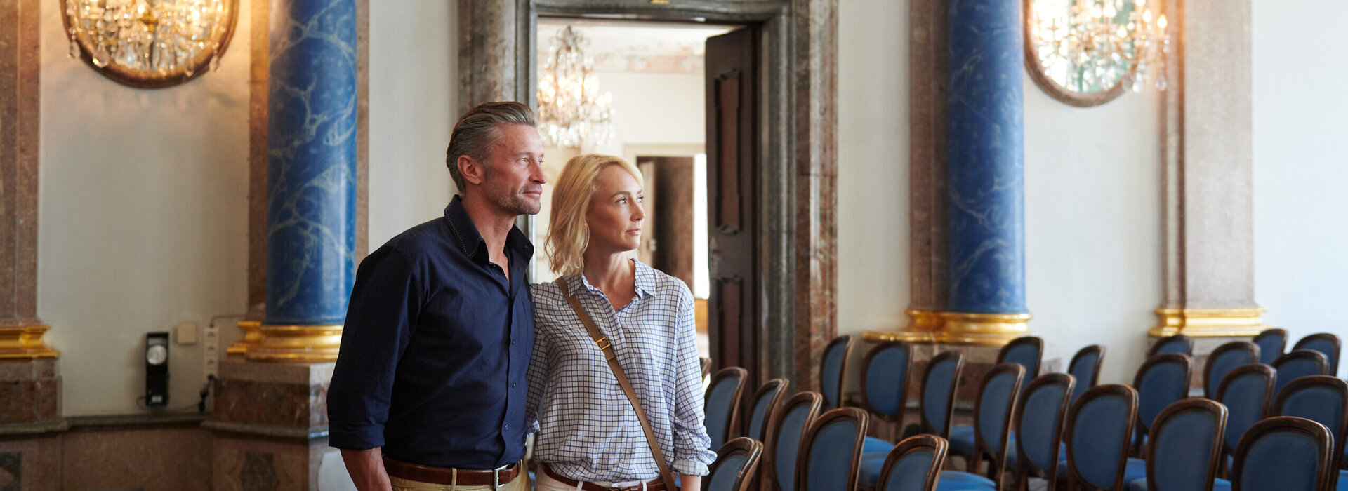 Besuch im Kaisersaal Ein Paar betrachtet die prunkvolle Innenausstattung eines Schlosses. Die Fassade beeindruckt mit blauen Säulen und Stuck.