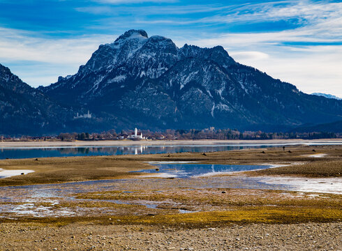 Zu den Veranstaltungsinformationen Blick über den teilabgelassenen Forggensee auf Schloss Neuschwanstein und den Säuling.