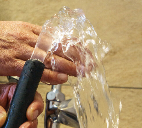 Das Bild zeigt zwei Hände die einen Wasserschlauch halten. Aus dem Wasserschlauch kommt ein klares Wasser, das über die eine Hand läuft.