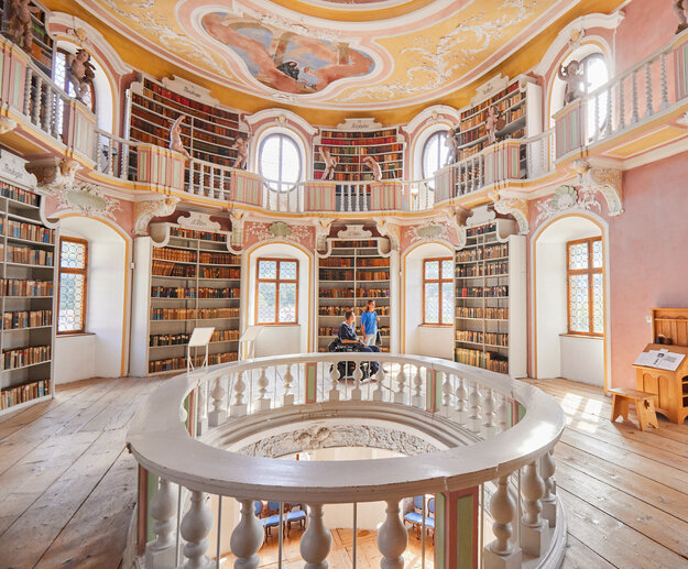 Ehemalige Klosterbibliothek Die Bibliothek des Hohen Schlosses in Füssen mit hohen Regalen und einem beeindruckenden Rundbogen. Das Bild zeigt einen Raum voller Wissen und Geschichte.