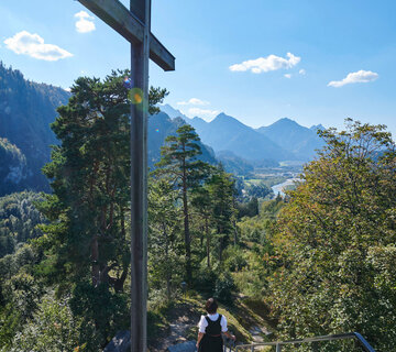 Eine Frau steigt Treppen am Kalvarienberg hinab, hinter ihr ein Gipfelkreuz