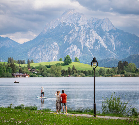 Spaziergänger auf der Uferpromenade in Hopfen am See, im Hintergrund der Säuling und das Ammergebirge