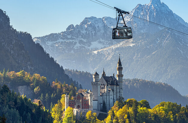 Eine Kabine der Tegelbergbahn gleitet am Schloss Neuschwanstein vorbei. Im Hintergrund ist der majestätische Säuling (2047m).