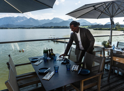 Zum Anderszeit-Blogbeitrag Das Foto zeigt die Terrasse vom Seehaus Hopfensee mit Blick auf den See und die Berge.
